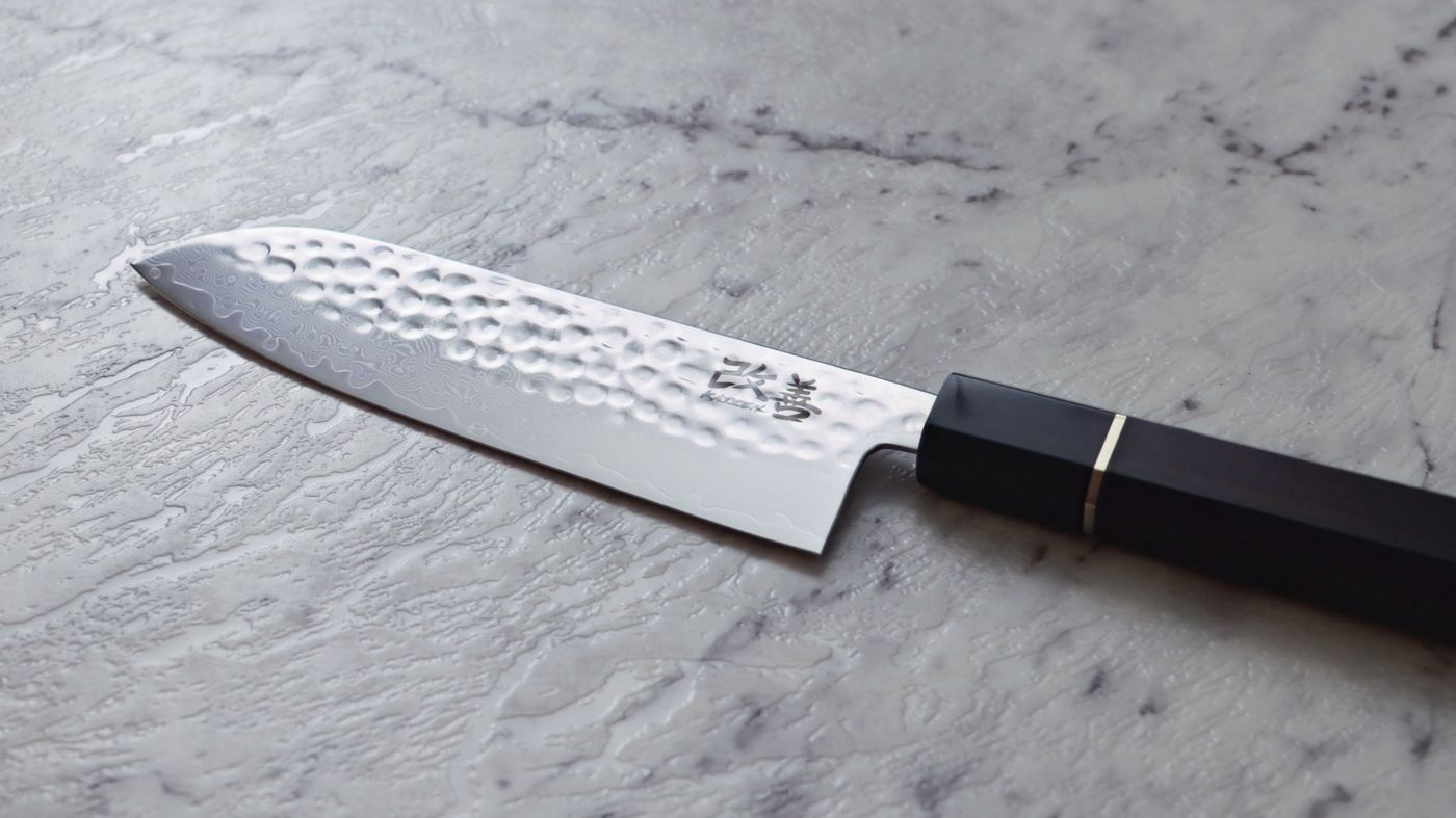 Close view of the Kaizen santoku on marble, hammered steel catching daylight